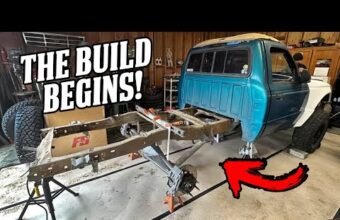 A garage with a truck being modified, the truck bed removed, exposing the frame and rear axle, and large off-road tires visible.