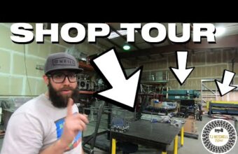 A person with a beard and glasses pointing upward in a workshop filled with tools and machinery. Arrows and the words shop tour are overlaid on the image.