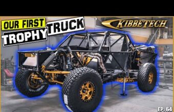 A partially built off-road trophy truck in a workshop with visible roll cage, tires, and suspension components, large text says our first trophy truck KibbeTech in the background, episode 64 displayed at the bottom corner.