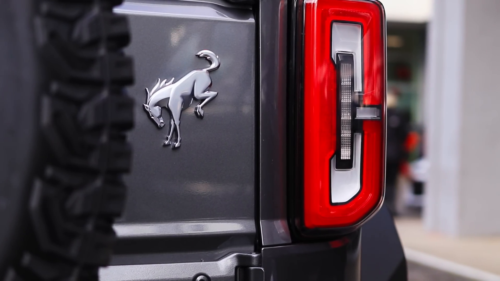 Rear view of a gray SUV with a red and white tail light, a silver horse emblem on the rear door, and part of a spare tire visible on the left.