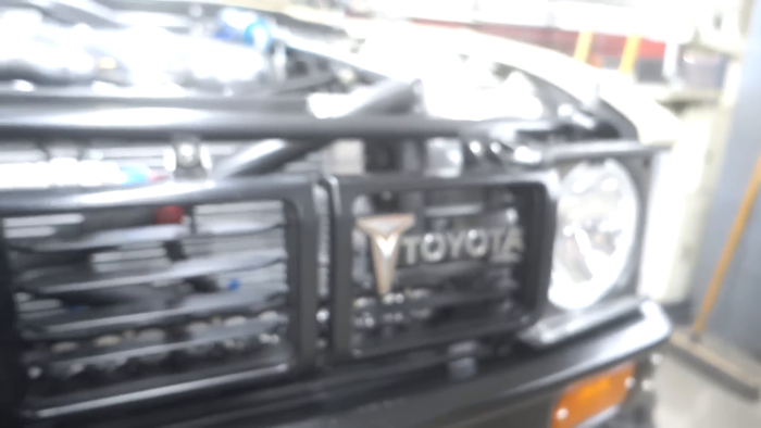 Front view of a Toyota vehicle with a grill and headlight visible, featuring a brush guard. The image focuses on the detailed design elements of the vehicle's front bumper area.